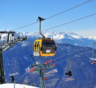 [Translate to englisch:] Gondel- und Sessellift in den verschneiten Alpen vor blauem Himmel.