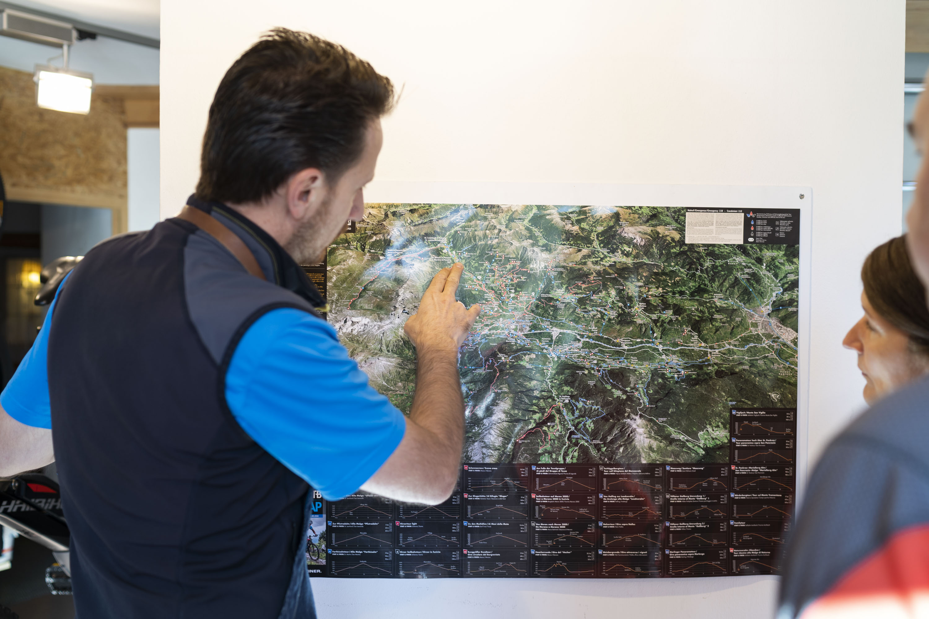 Mann zeigt auf eine Landkarte an der Wand, zwei Personen schauen zu