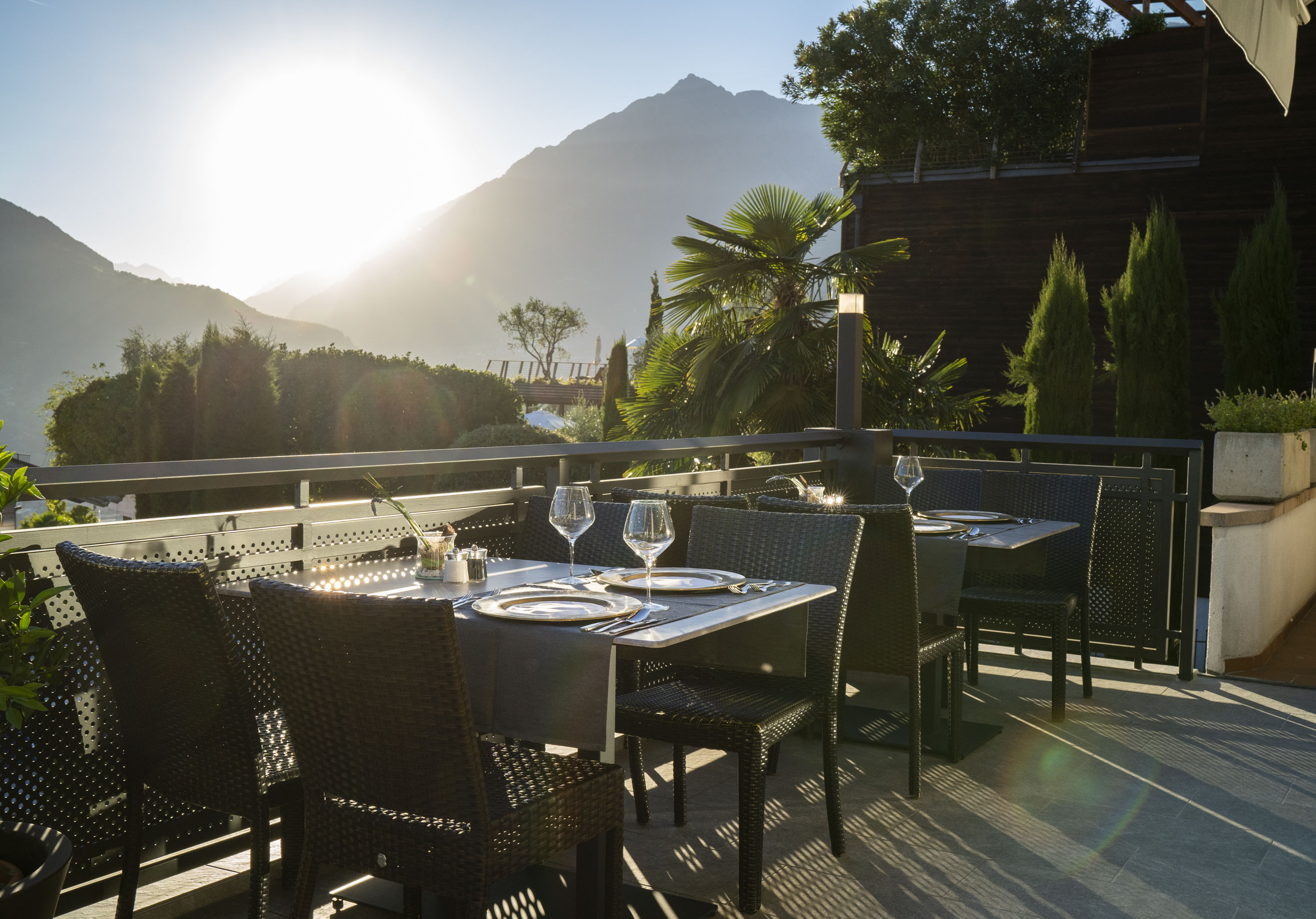 Sonnige Terrasse mit gedeckten Tischen und Stühlen, im Hintergrund Berge und Pflanzen.