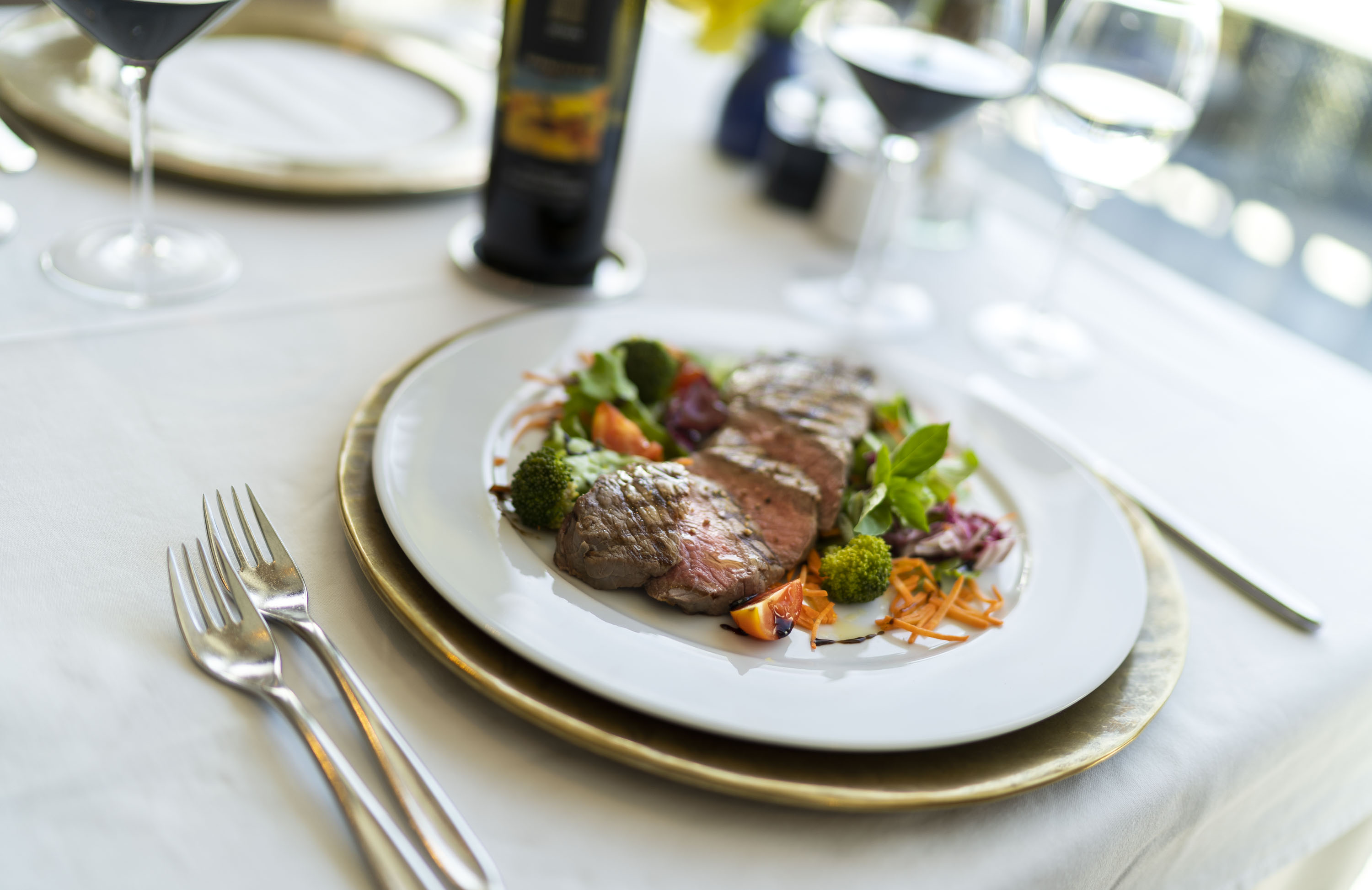 Elegante gedeckte Tafel mit einem Teller saftig gegrilltem Fleisch und Gemüse, daneben Wein und Besteck.