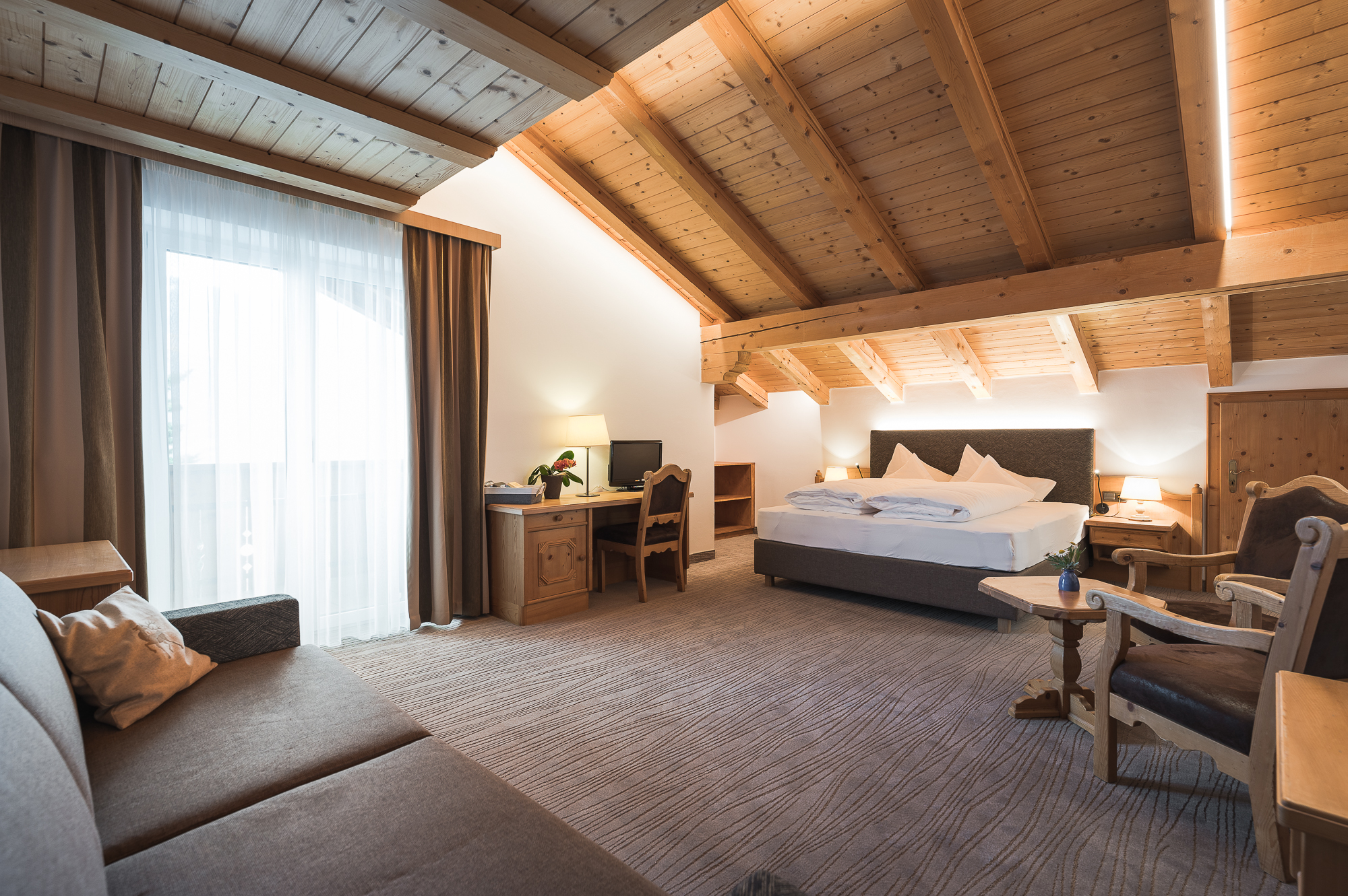 Gemütliches Hotelzimmer mit Holzdecke, Doppelbett, Schreibtisch, Sofa und zwei Sesseln