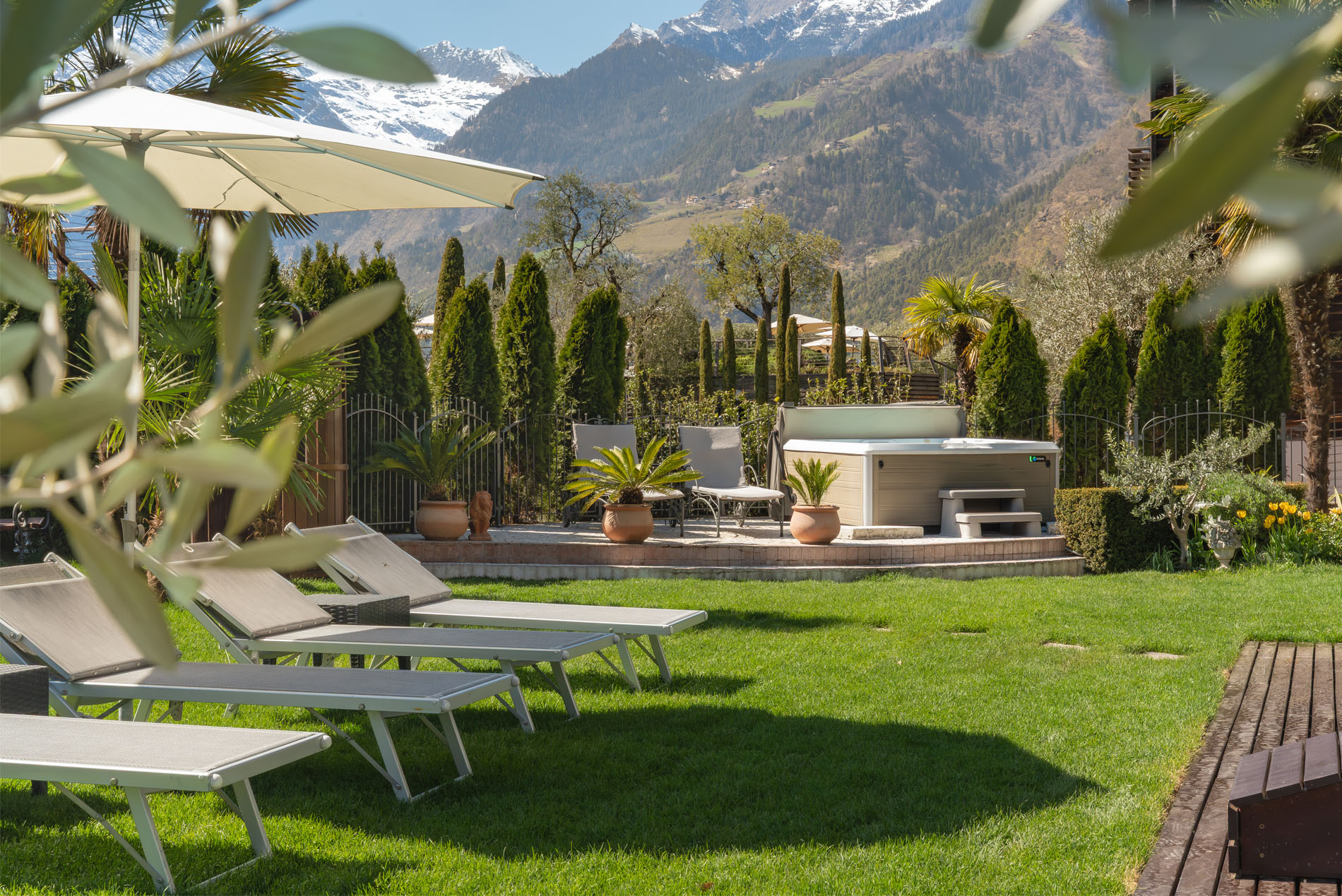 Garten mit Liegestühlen, Sonnenschirm, Whirlpool und Blick auf schneebedeckte Berge im Hintergrund